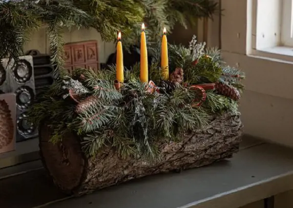A traditional Yule Log decorated with green leaves and vines with three candles burning on top.