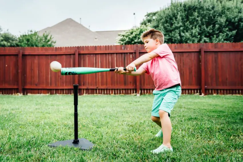 A kid enjoys playing with a tee ball set in his backyard