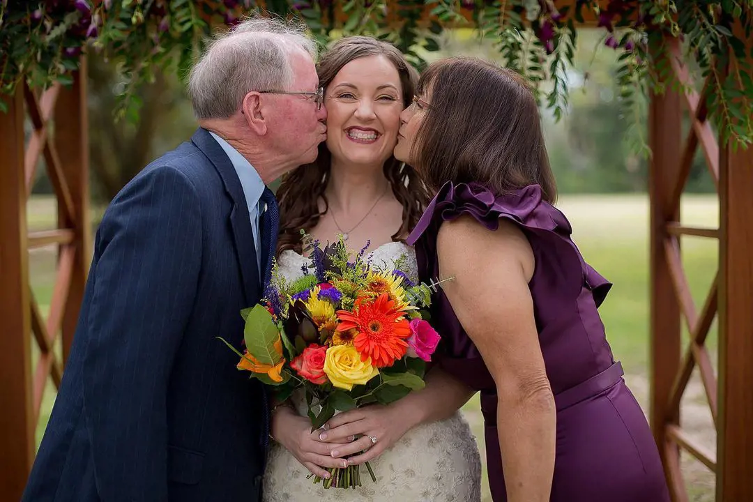 Father and mother embrace their daughter on her wedding day while photographer Jenifer Zambiazzi captures the moment