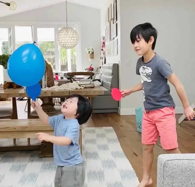 Two boys playing balloon tennis with mini-sized ping pong rackets in the living room