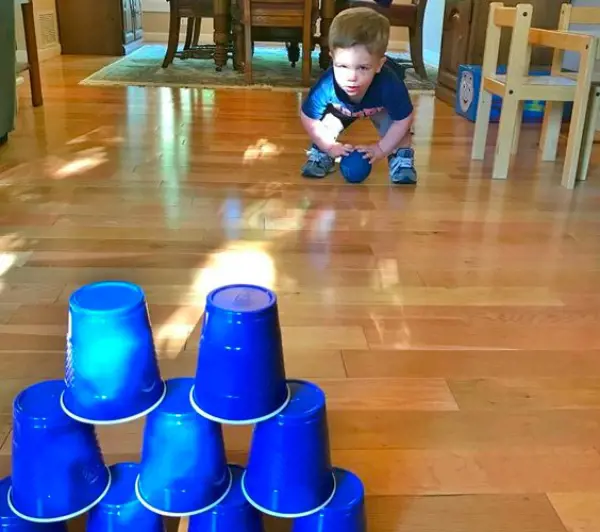 A toodler takes aim at the stacked pyramid of paper cups with a ball in his hands