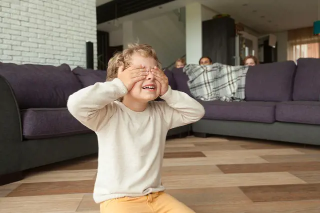 A kid covers his eyes as he makes count down while other family members find a place to hide