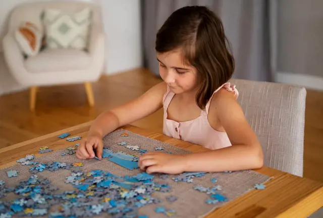 A child is carefully putting the pieces of a puzzle together to build the original picture