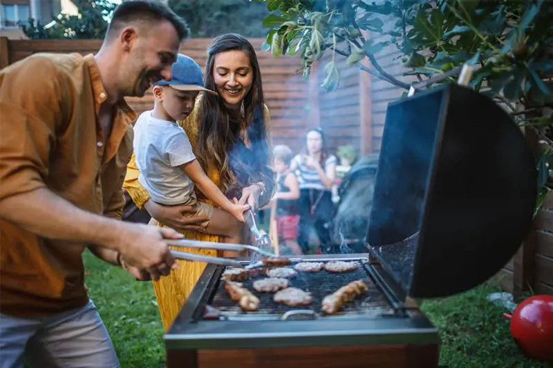 Family enjoying an outdoor barbecue grilling sausages and steaks