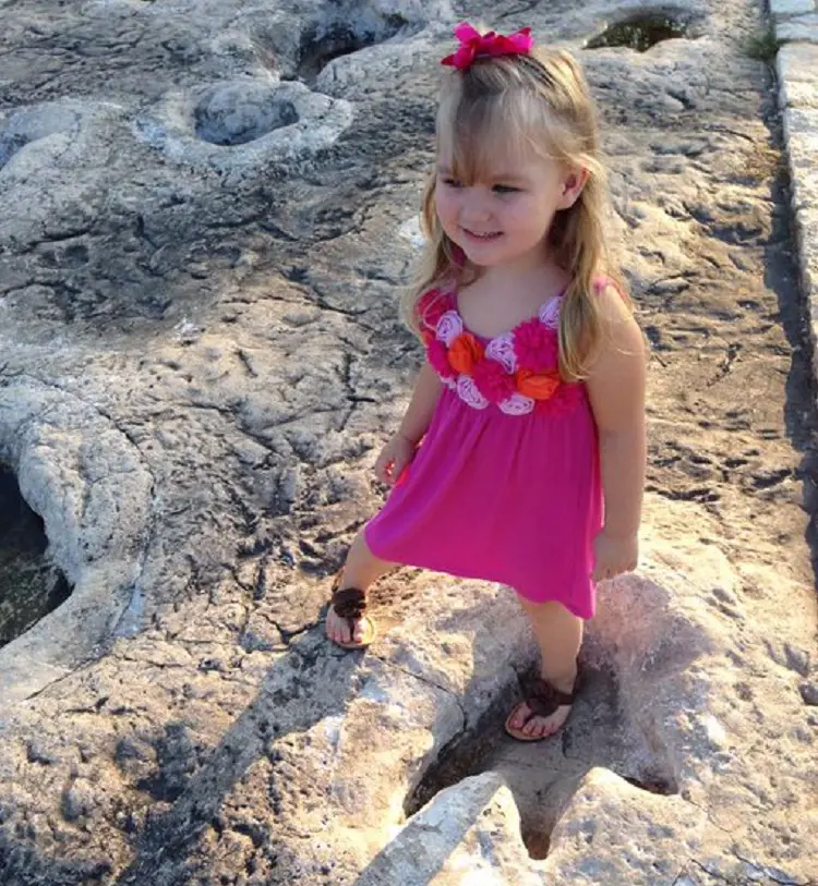 A little girl comparing her footprint with a huge dinosaur footprint on the riverbed at Glen Rose.