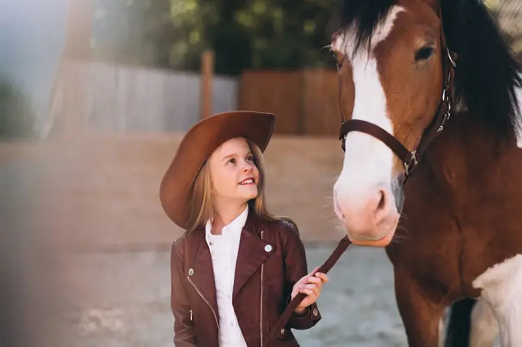 A little girl experiencing wild west wearing a cowboy hat with a horse. 