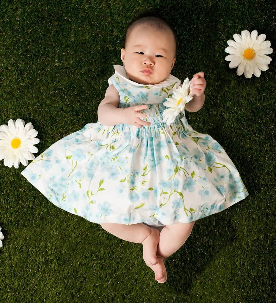 A sweet baby girl holds a daisy flower in her hand while lying in the grass creating an adorable picture