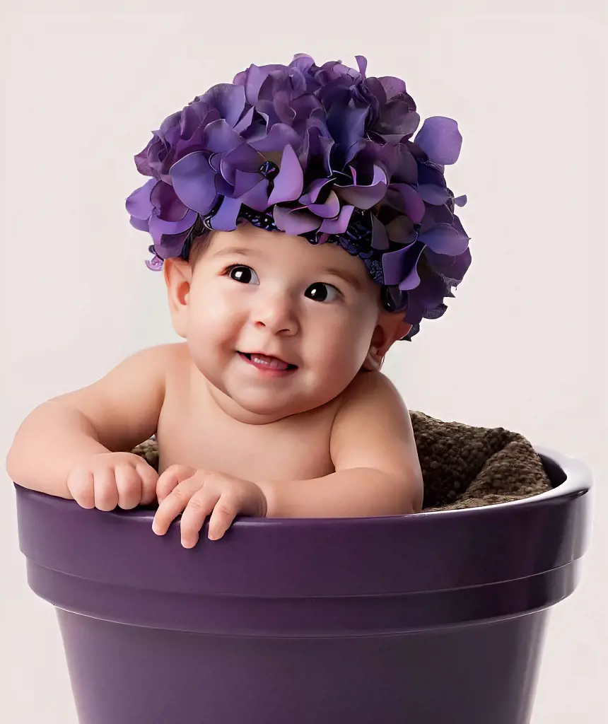 The adorable baby girl sits in a vase filled with violet flowers, wearing a crown made of violet flowers, and smiles beautifully