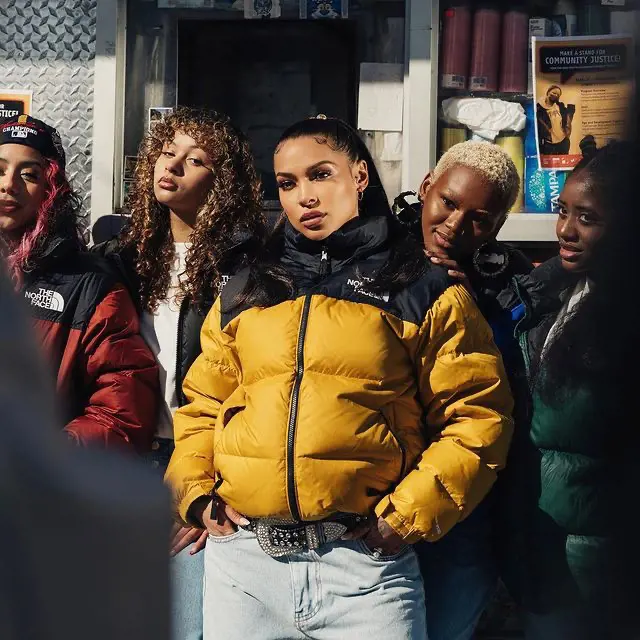 Nokia poses in a retro nuptse jacket and jeans with the crew of her new music video in 2022