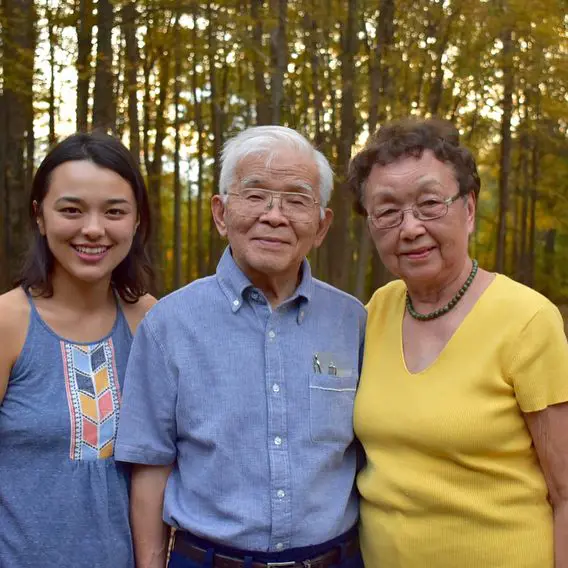 Midori with her grandparents as they look into the camera with a joyful expression
