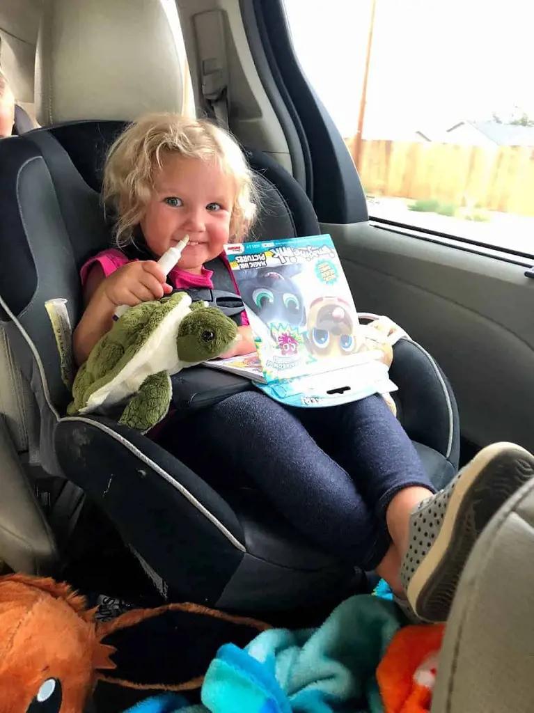 A toddler in car holding storybook and toys